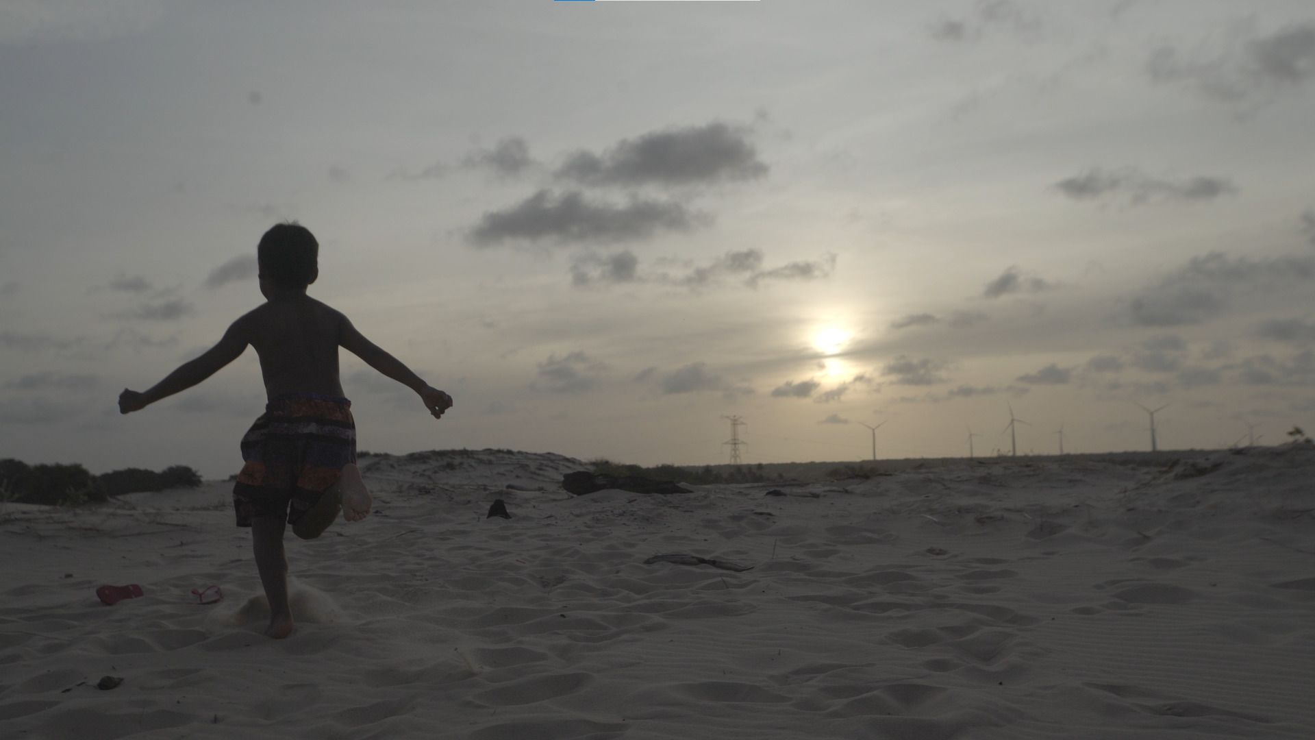 No canto esquerdo da imagem, vemos um garoto correr em uma praia. No canto esquerdo da imagem, vemos um garoto correr em uma praia.